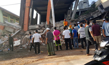 Người dân đứng quanh những tòa nhà bị đổ sập sau trận động đất mạnh 6,5 độ Richter ở Ule Glee, Pidie Jaya thuộc tỉnh Aceh, Indonesia.